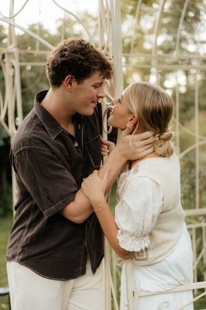 A couple leans in for a close romantic moment under a white metal arbor in a garden setting.