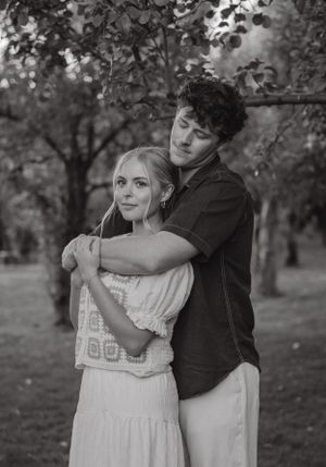 Black and white portrait of a couple embracing tenderly under a canopy of trees in an orchard.