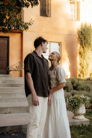 Couple sharing a romantic moment outside a golden-hued building, woman in white dress gazing up at partner.
