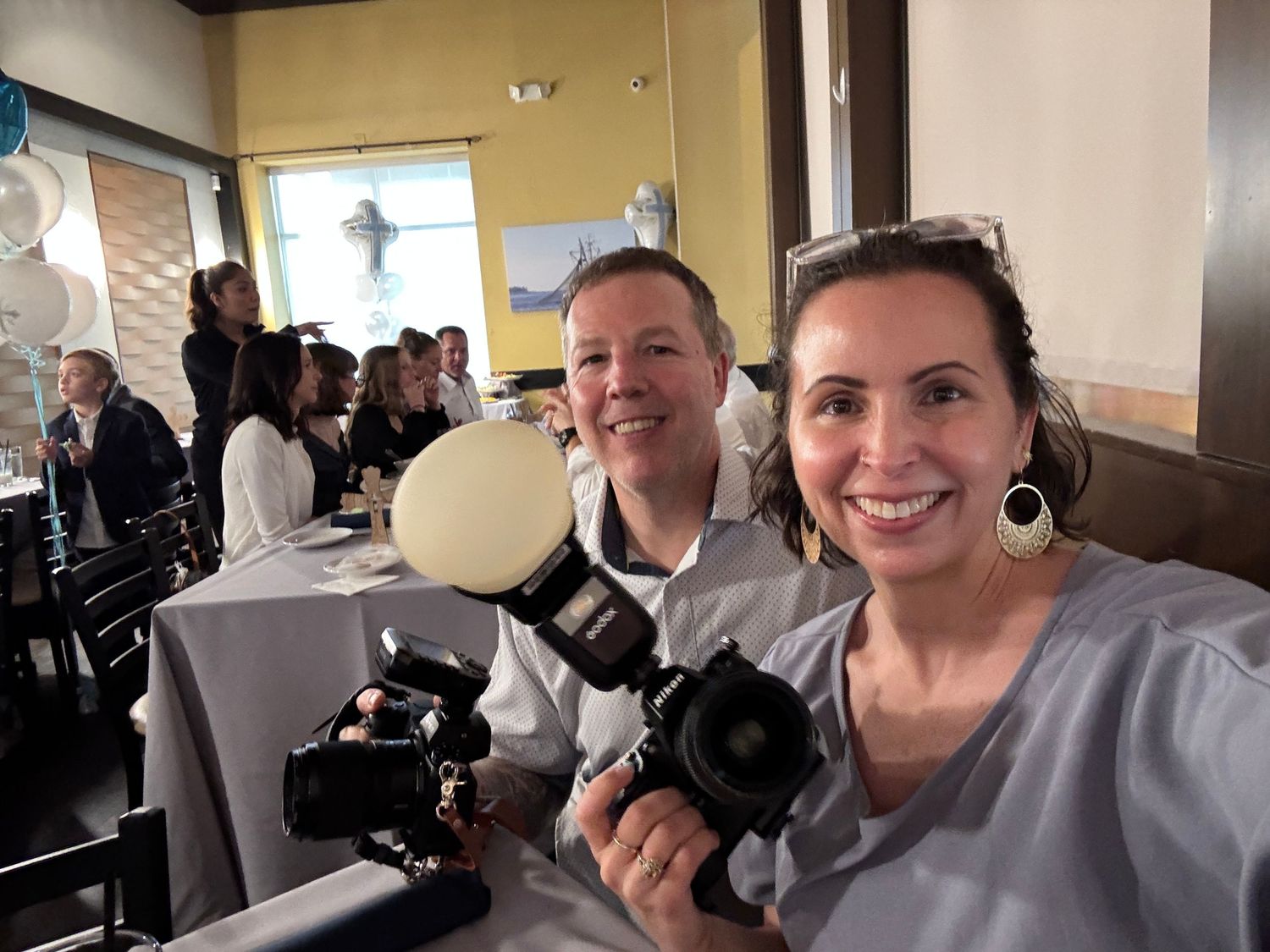 Two photographers sitting together at a restaurant showing their professional cameras during an event.