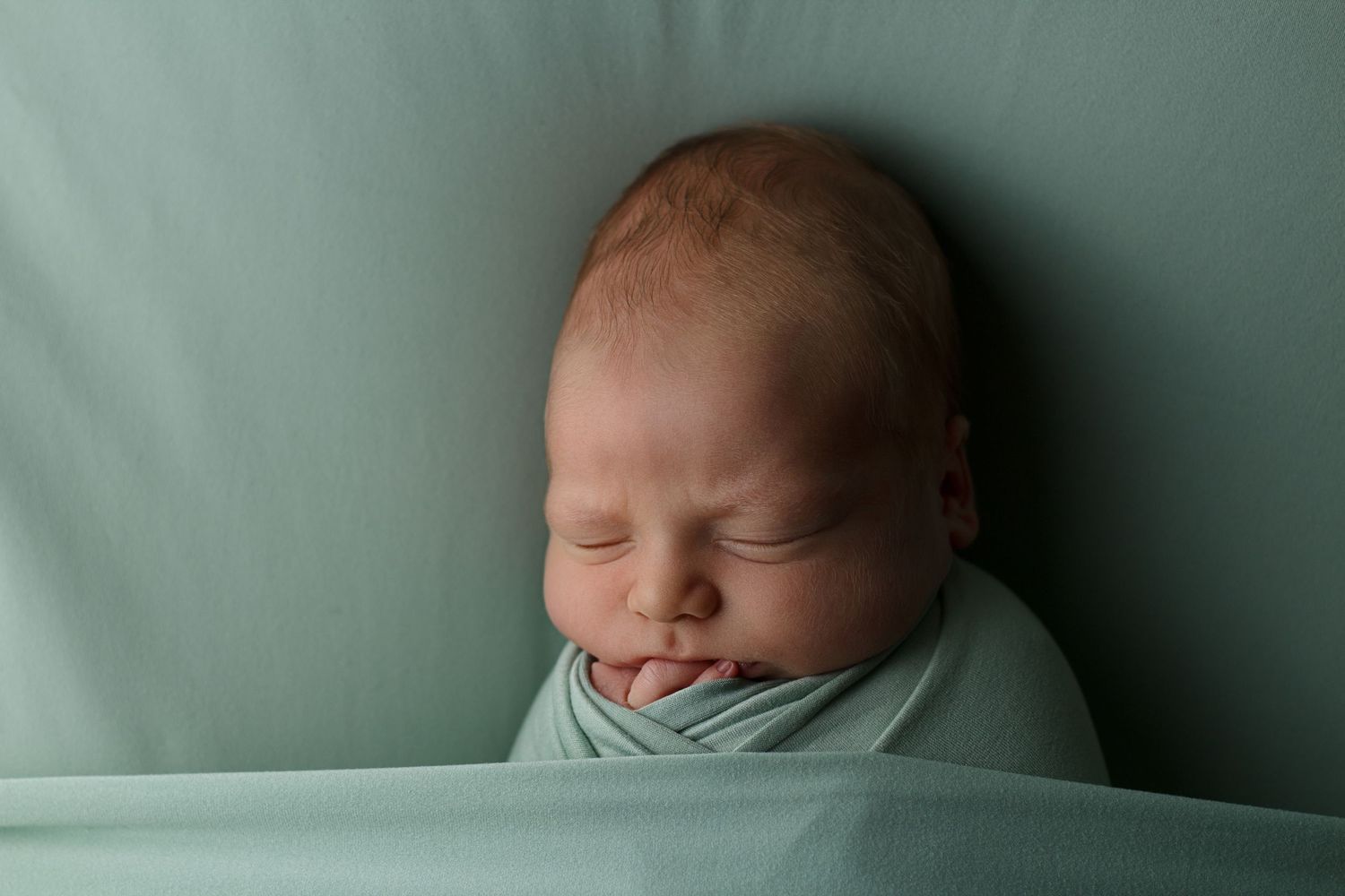 Peaceful sleeping newborn baby swaddled in soft mint green wrap.