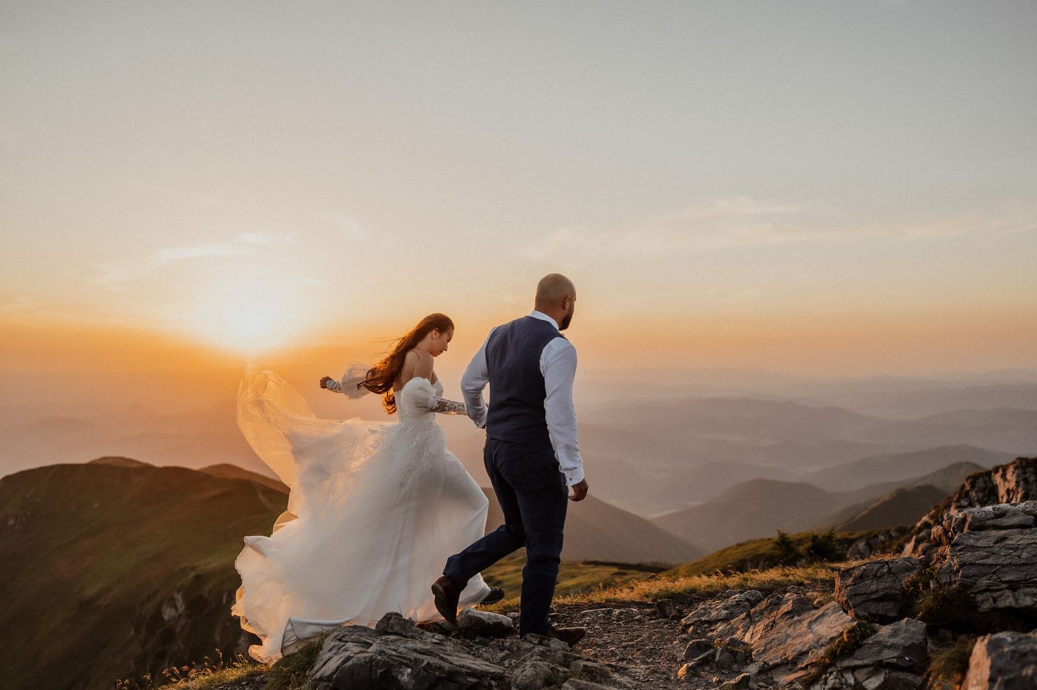 Dramatic sunset mountain top wedding portrait with bride's dress flowing in the wind.