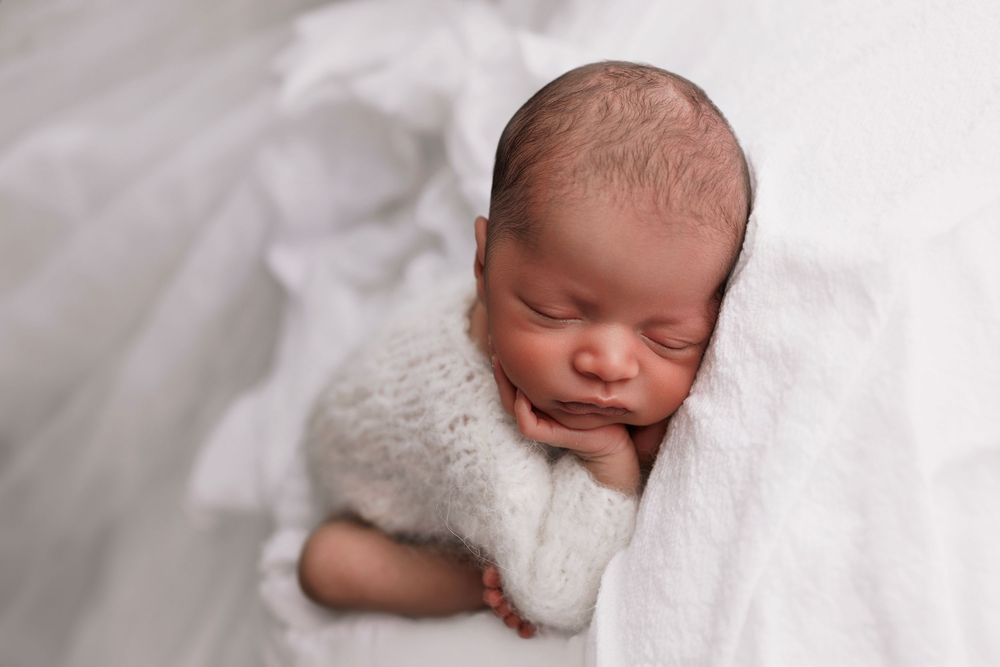 Peaceful newborn baby sleeping on soft white blanket during professional portrait session.