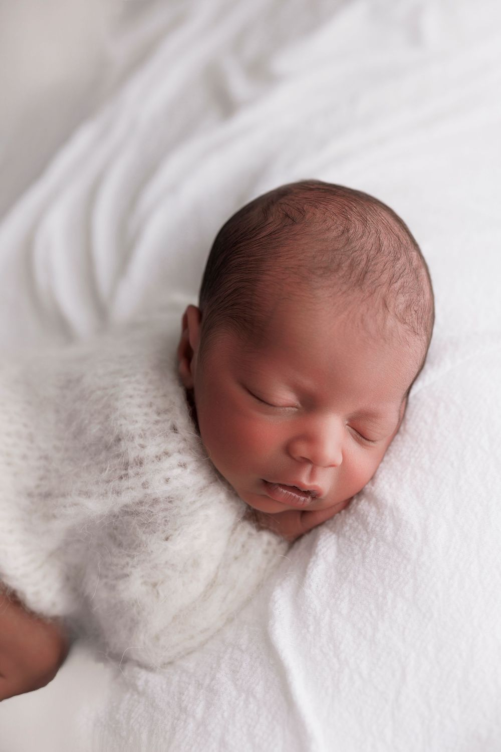 Peaceful newborn baby sleeping on soft white blanket during professional photography session.