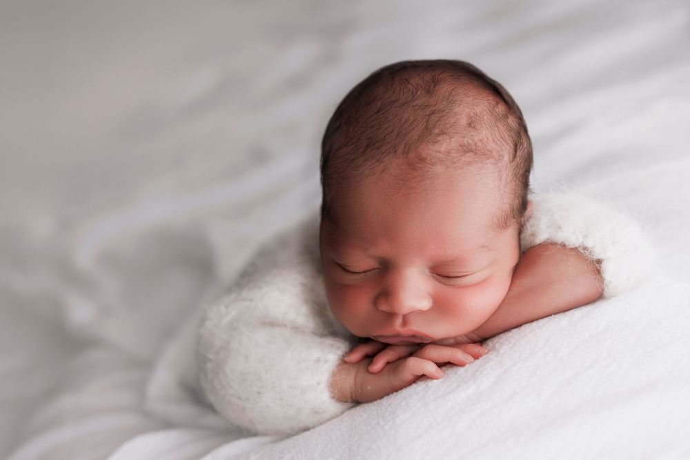 Sleeping newborn baby rests peacefully on soft white blanket during professional portrait session.