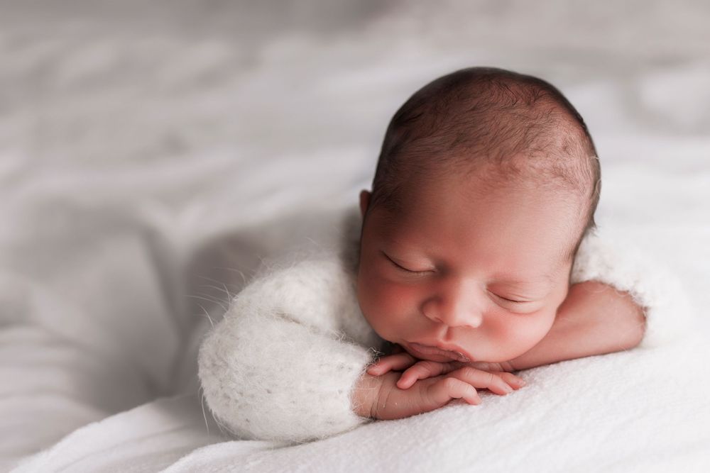 Peaceful sleeping newborn baby resting on soft white bedding with hands tucked under cheek.
