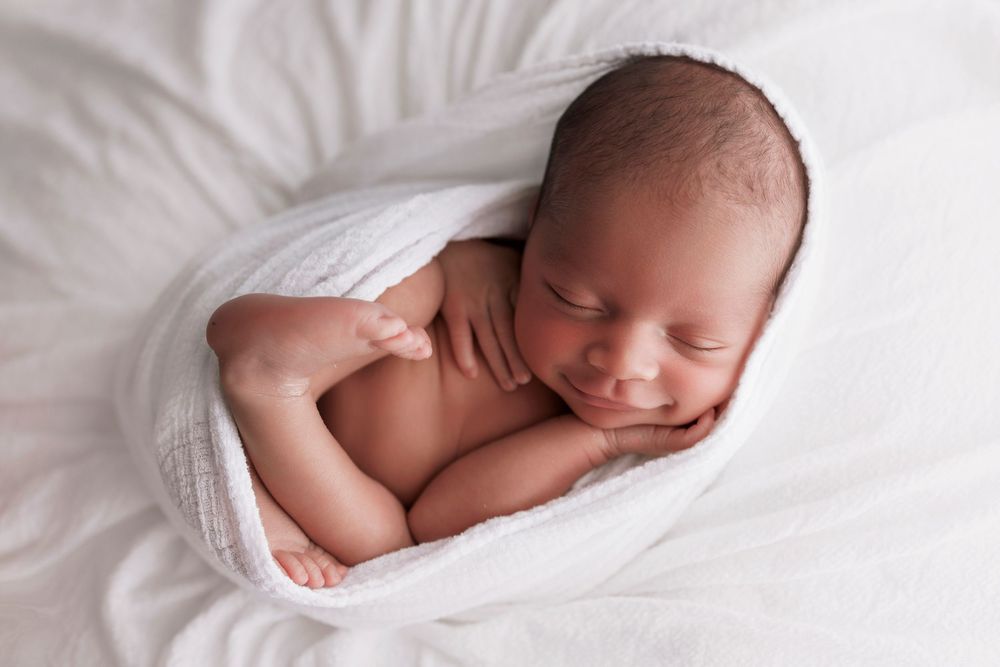 Sleeping newborn baby curled up on soft white blanket during peaceful studio portrait session.