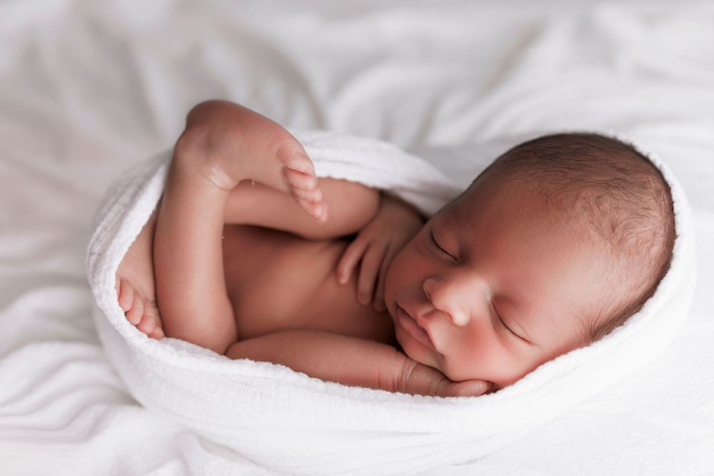 Peaceful newborn baby sleeping on soft white blanket in curled up position.