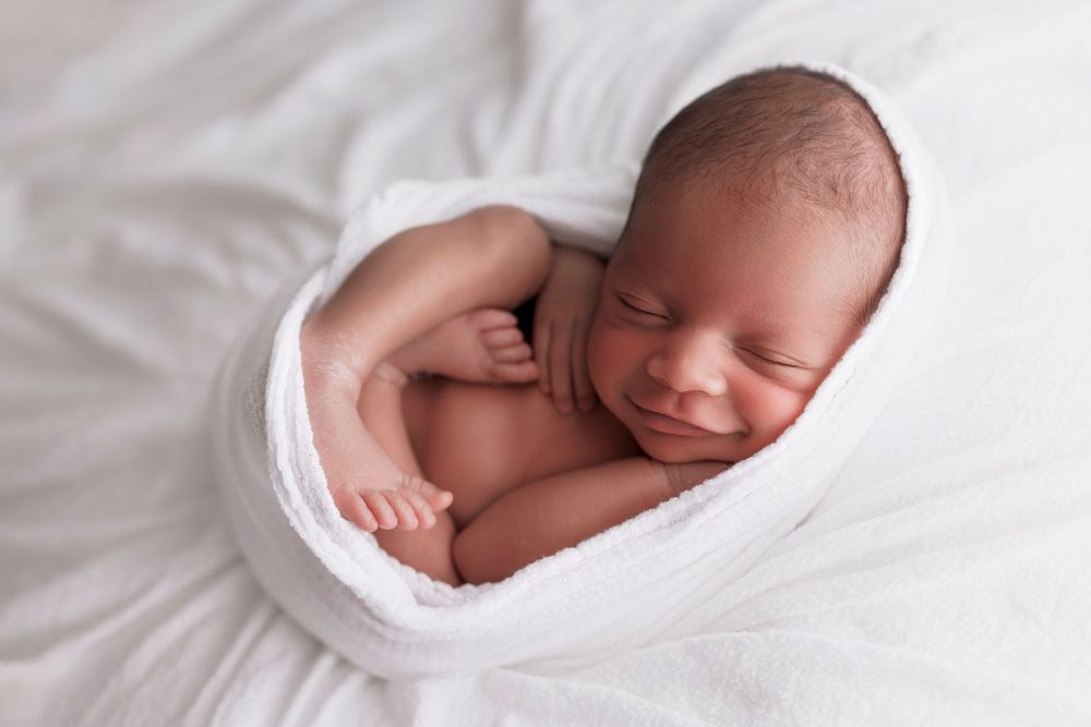 Sleeping newborn baby swaddled in white fabric during professional portrait session.