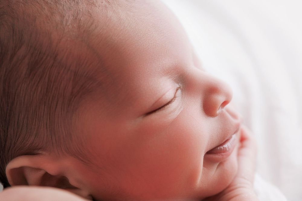 Peaceful sleeping infant with rosy cheeks shown in closeup profile against soft white background.