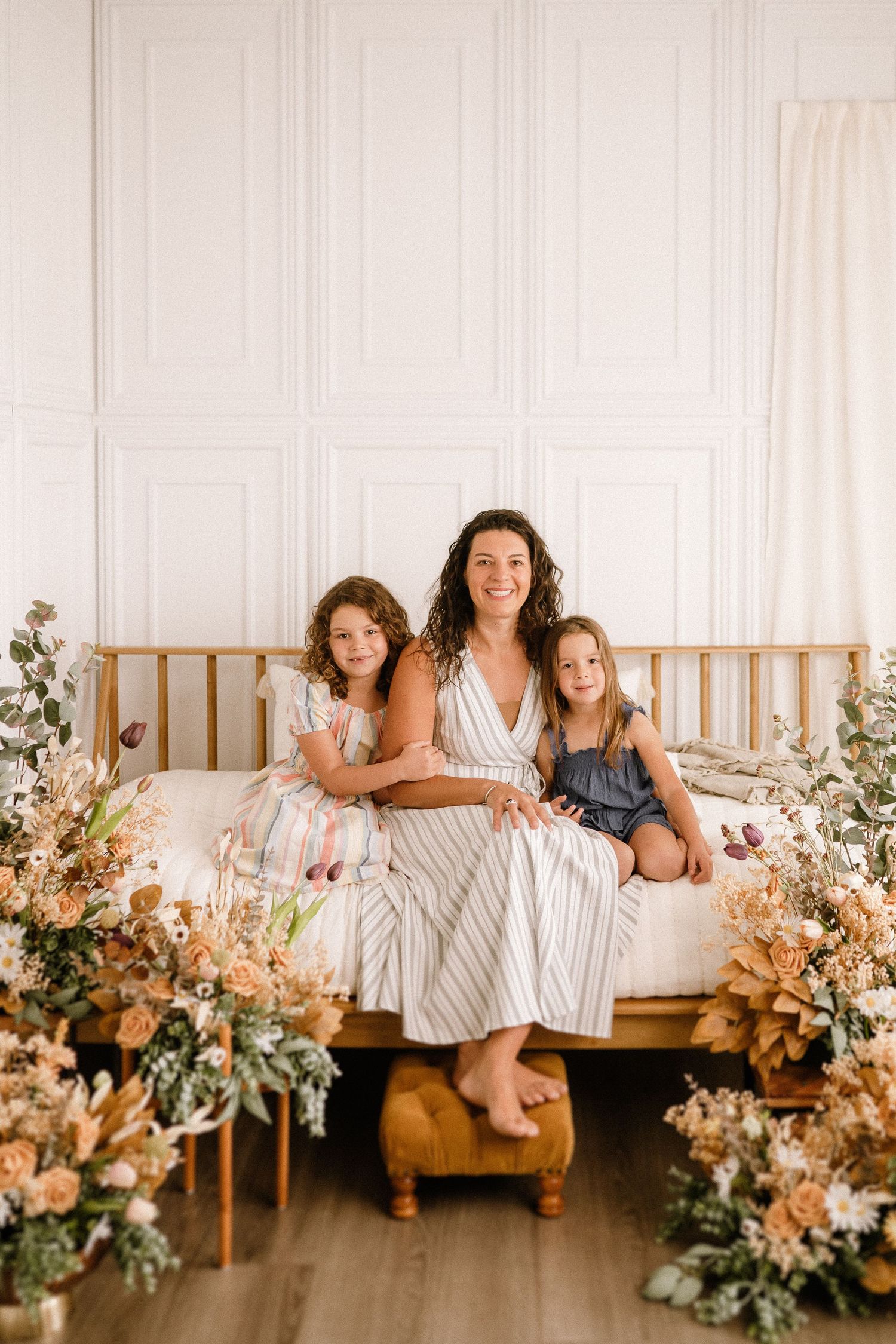 Family photo session featuring white walled room decorated with dried flowers and wooden bench.