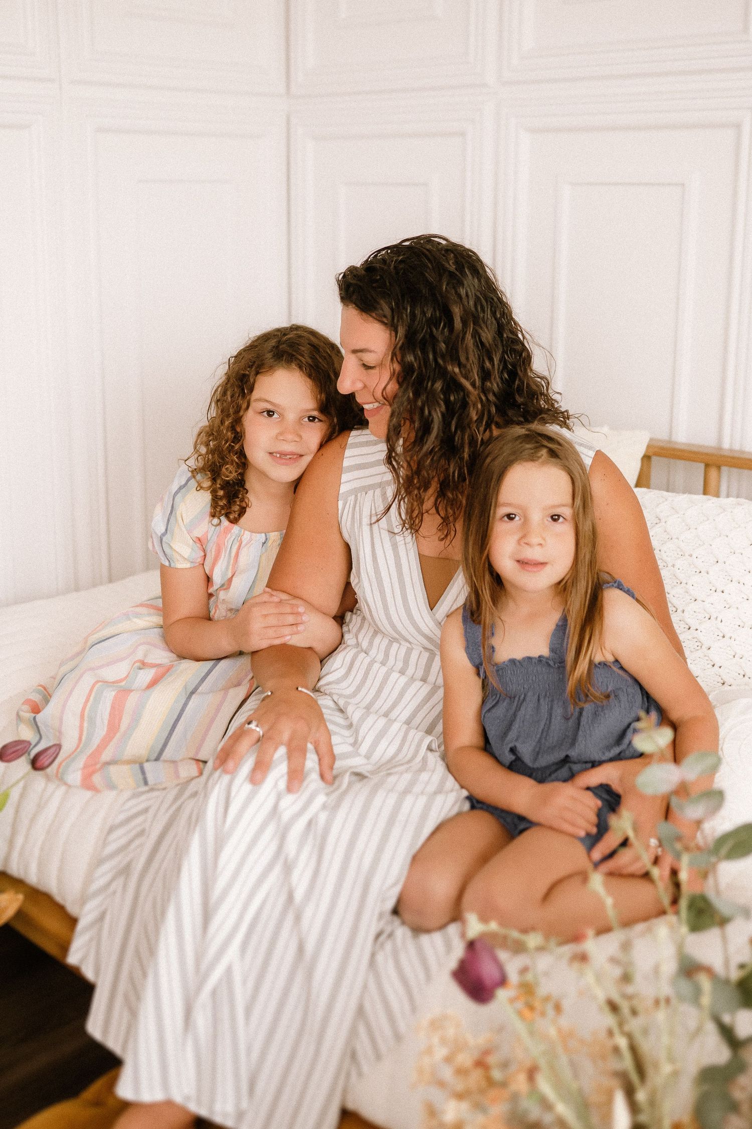 Sweet family moment captured on bed with matching white and striped outfits and natural curly hair.
