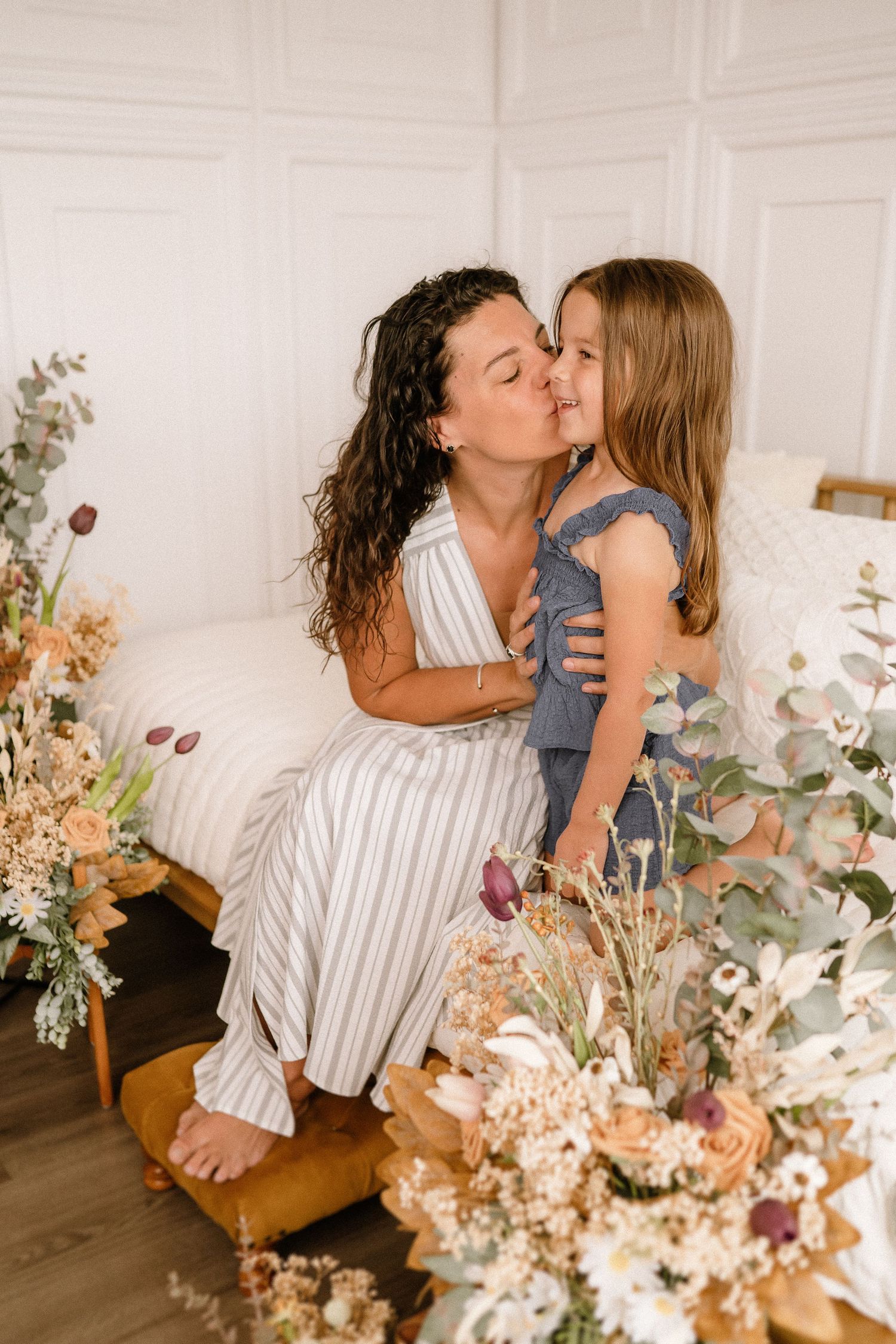 Two people share an intimate moment surrounded by dried floral arrangements in a bright white room.