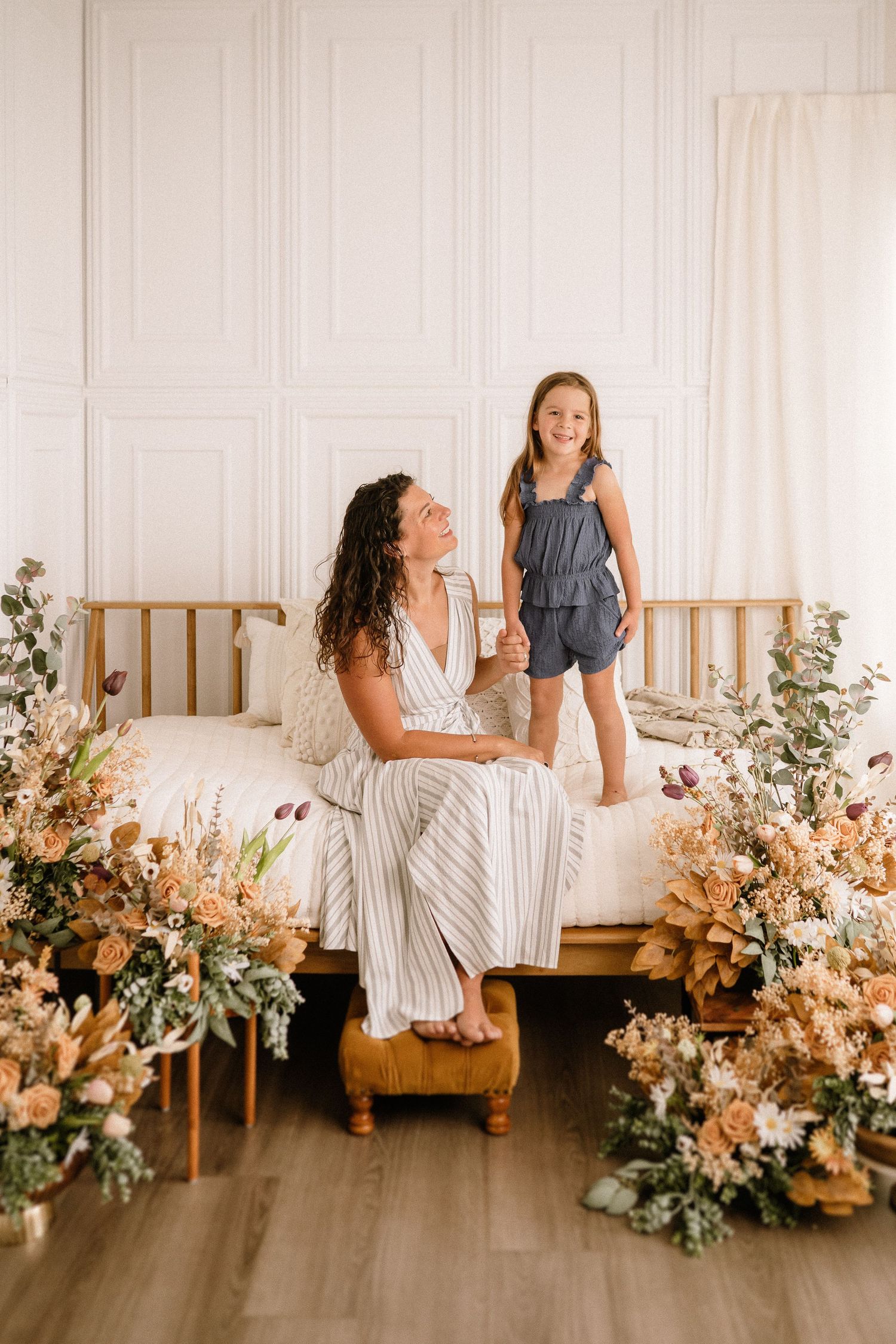 A whimsical indoor scene with dried floral arrangements surrounding a wooden bench in a bright white room.