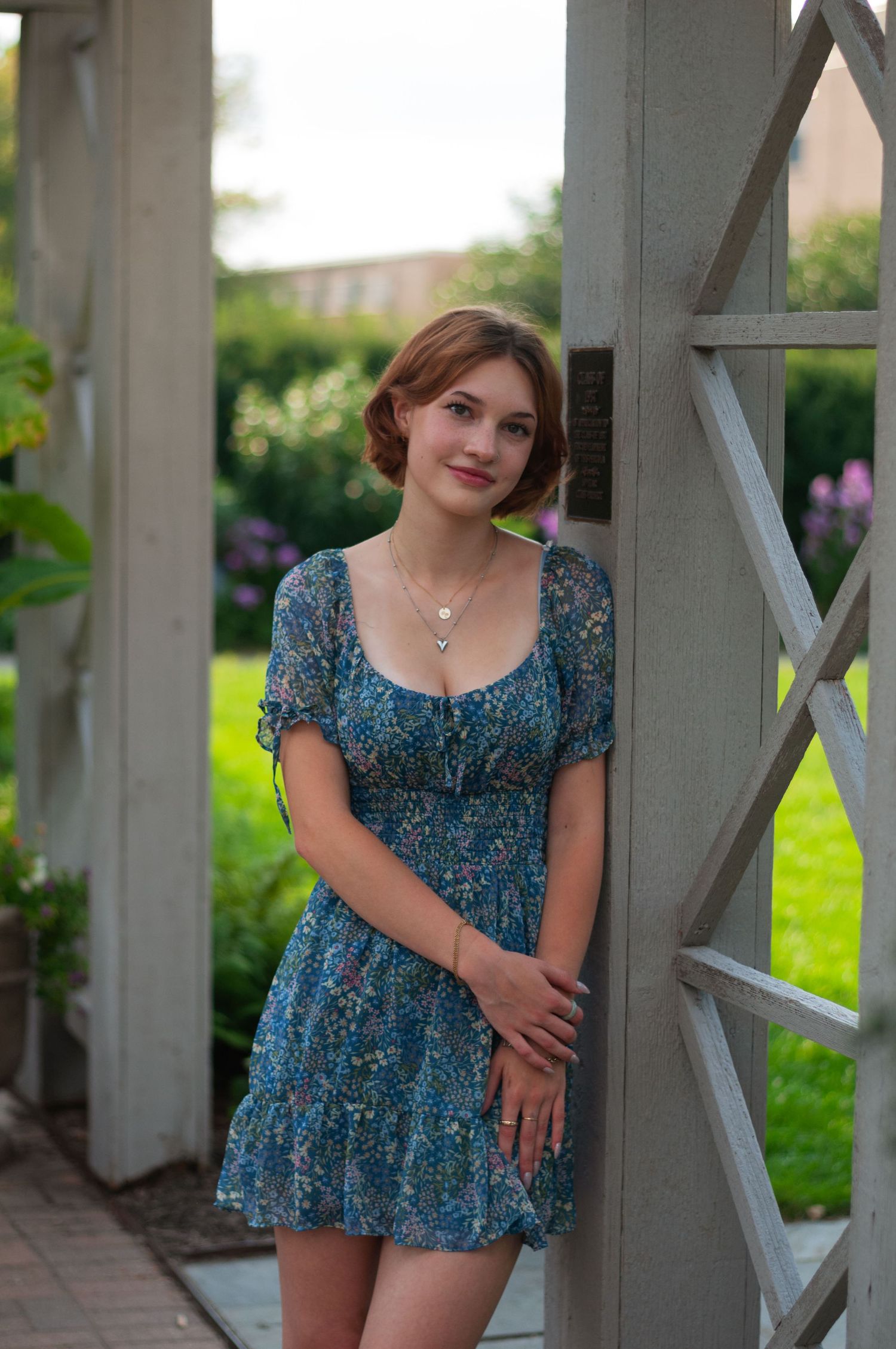 Senior girl in a blue dress leaning against a trellis with greenery in the background