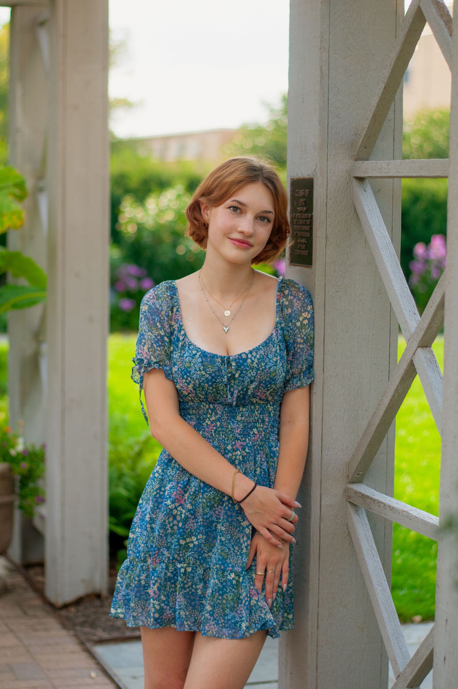 Senior girl in a blue dress leaning against a trellis with greenery in the background