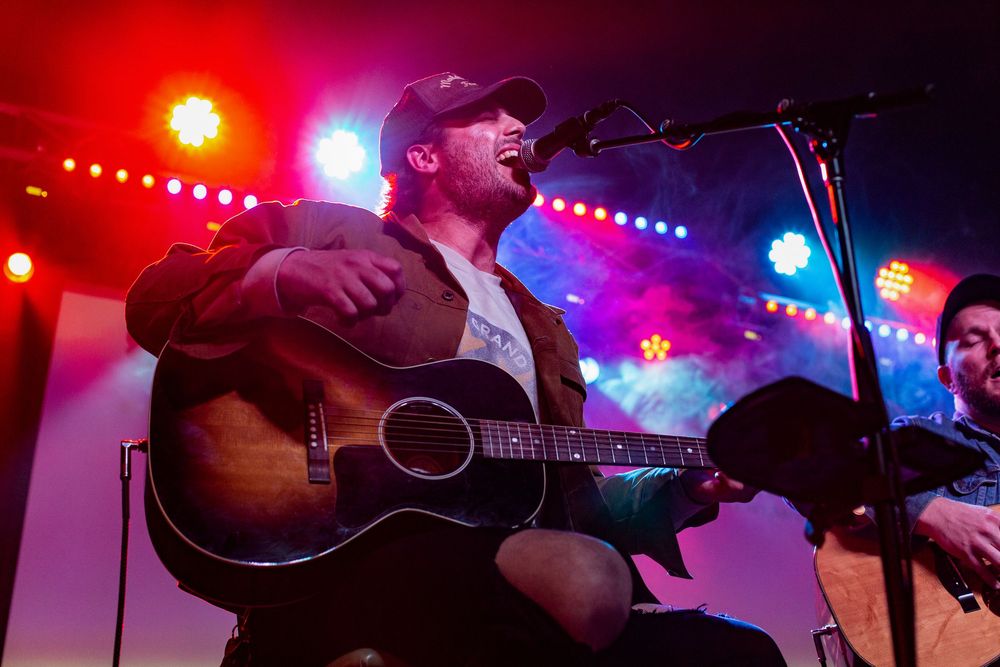Musician Jackie Lee performs on acoustic guitar under vibrant red and blue stage lighting at indoor concert venue Live Oak Nashville.
