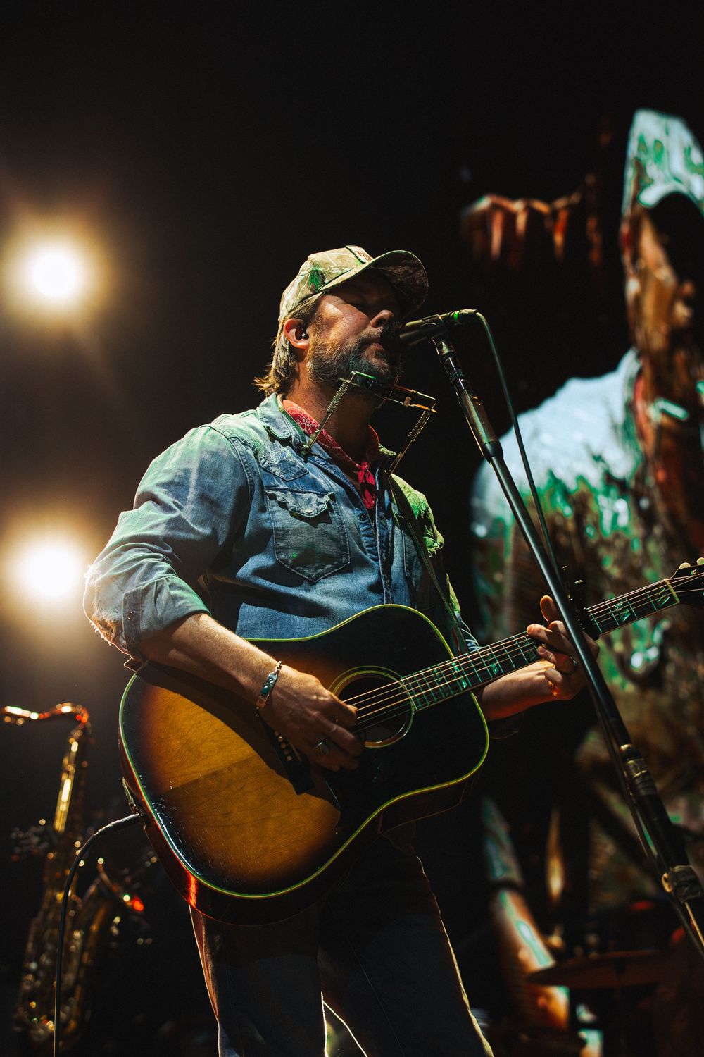 Christian artist Zach Williams playing acoustic guitar and singing into microphone on stage under warm spotlights.