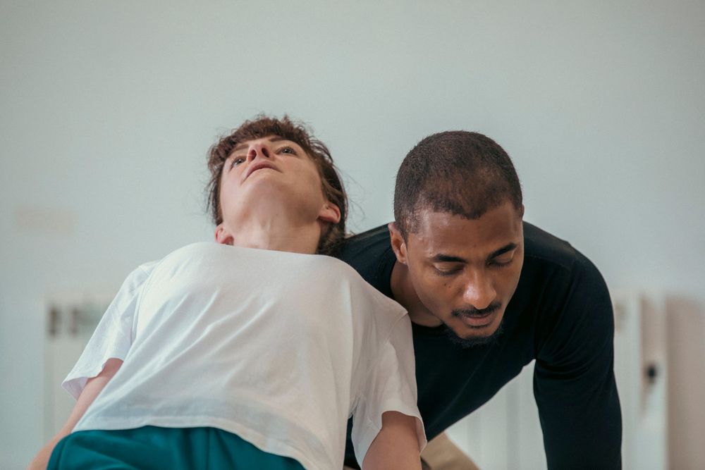 Two dancers perform an expressive contemporary dance move against a light background.