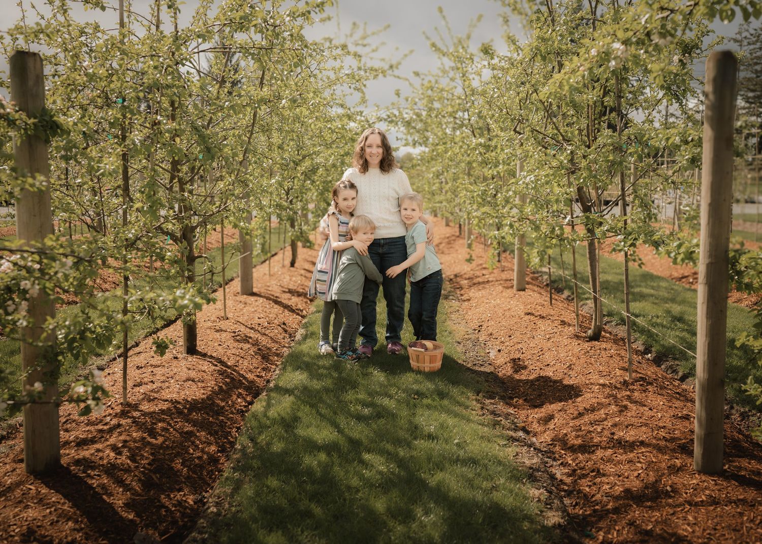 Person standing in an orchard with gardening supplies during golden hour.
