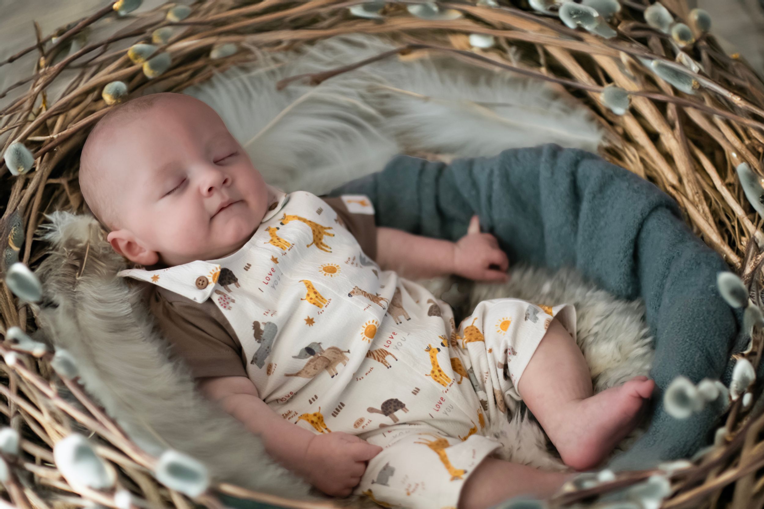 A sleeping baby rests peacefully in a woven basket wearing a white onesie with orange fox print patterns.