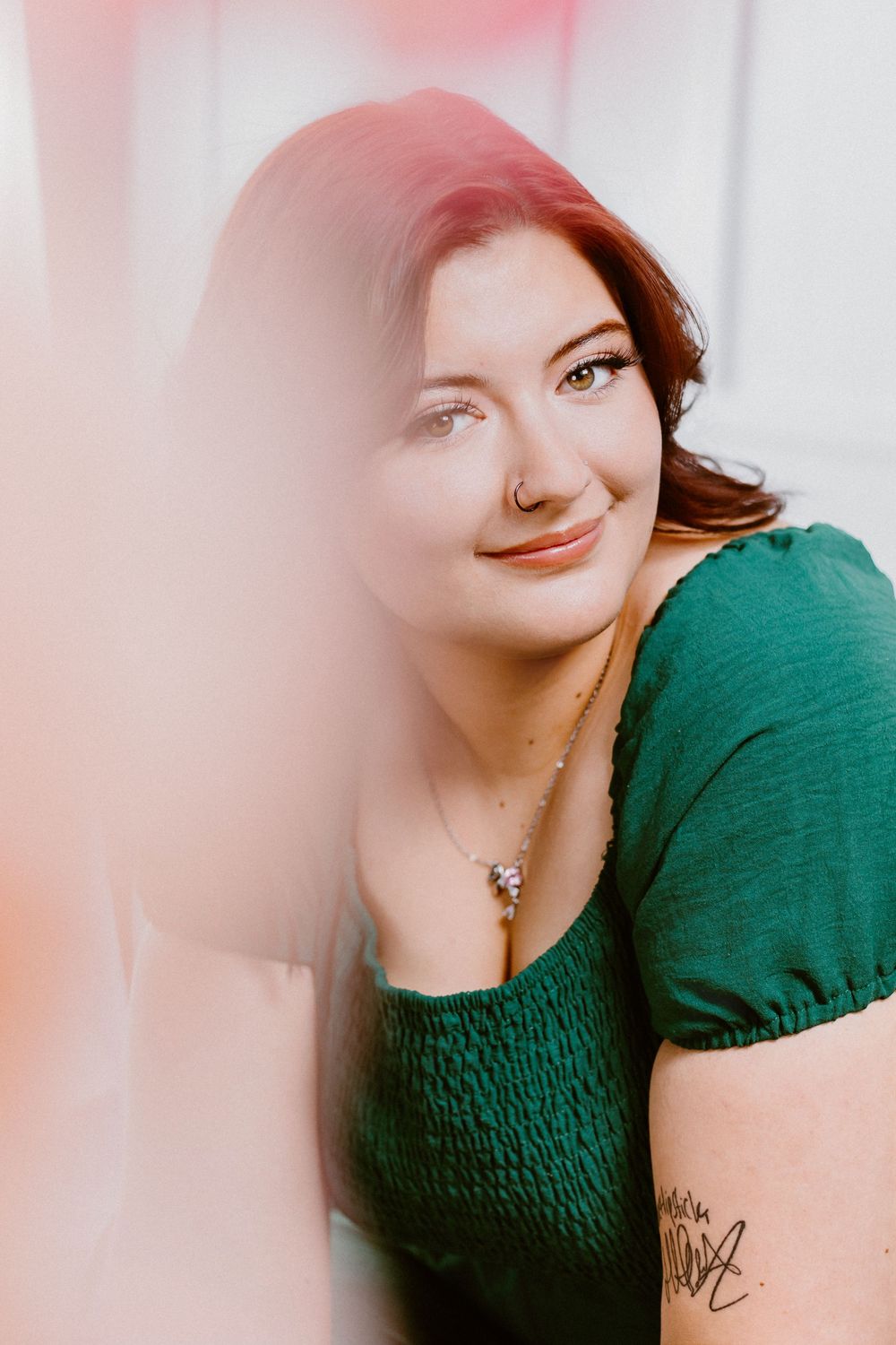Portrait in soft lighting wearing emerald green top with delicate necklace.