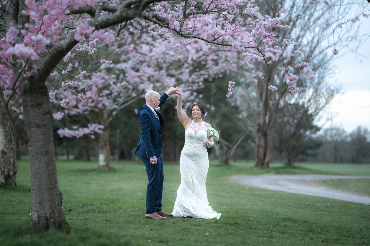 Wedding couple standing under blooming cherry blossom trees in spring garden.