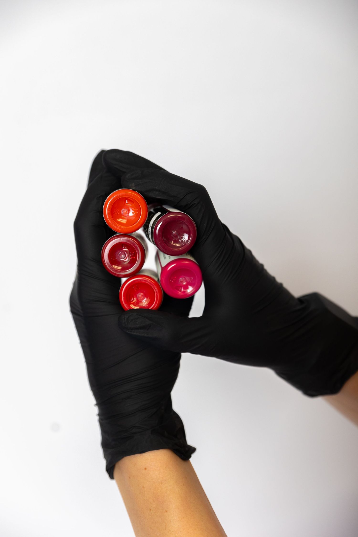 Hands wearing black gloves holding collection of red and pink lip products.