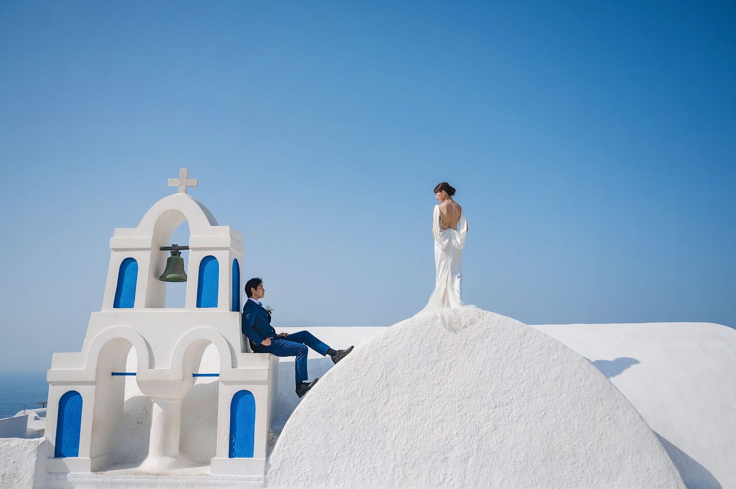 A couple poses near a white church with blue domes in Santorini, Greece.