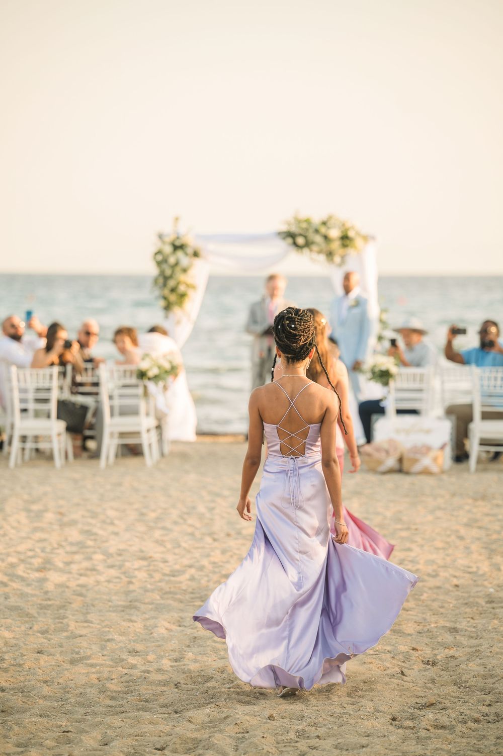 Elegant beach wedding scene with flowing dress and white decor against seaside backdrop.