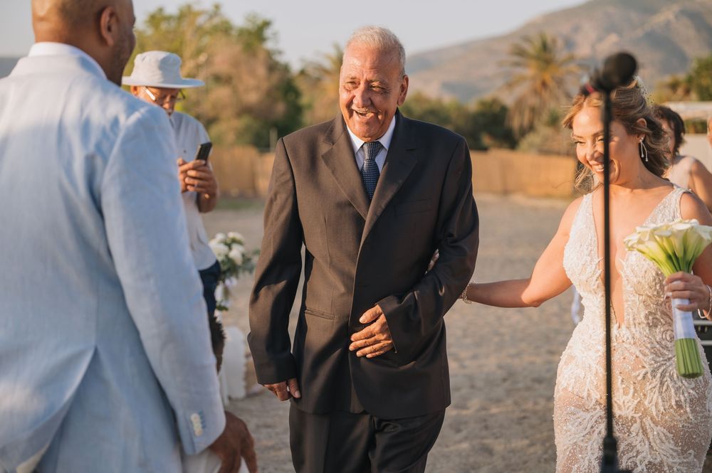 An outdoor beach wedding processional with guests and attendees gathered on the sand.