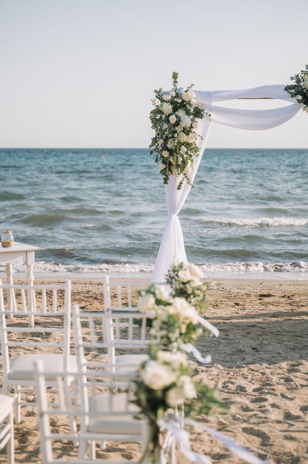 Elegant beach wedding arch with white draping and floral arrangements overlooking the ocean.