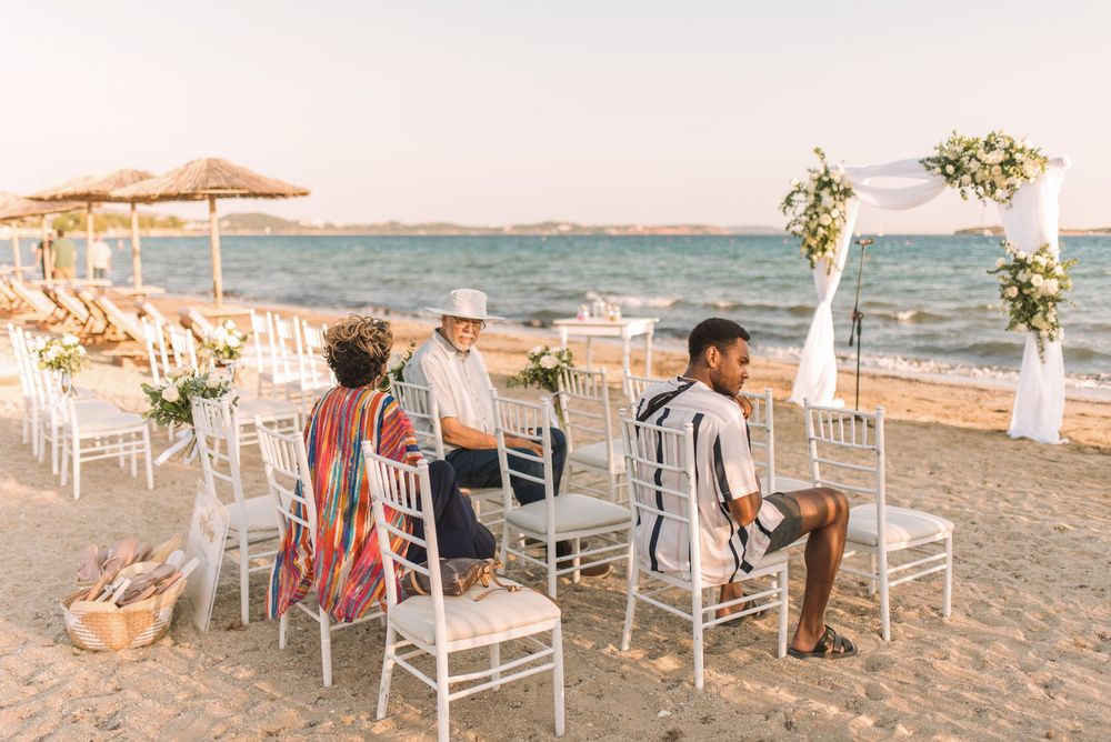 Beach wedding setup with white chairs and bamboo umbrellas facing ocean view.