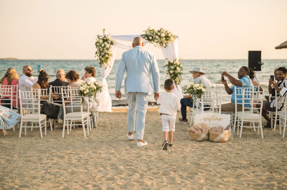 Beachside wedding ceremony with white chairs and floral arch against ocean backdrop.