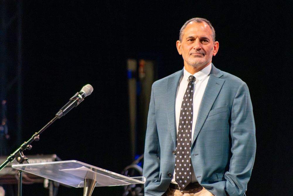 Speaker in light blue suit presenting at podium during professional conference.