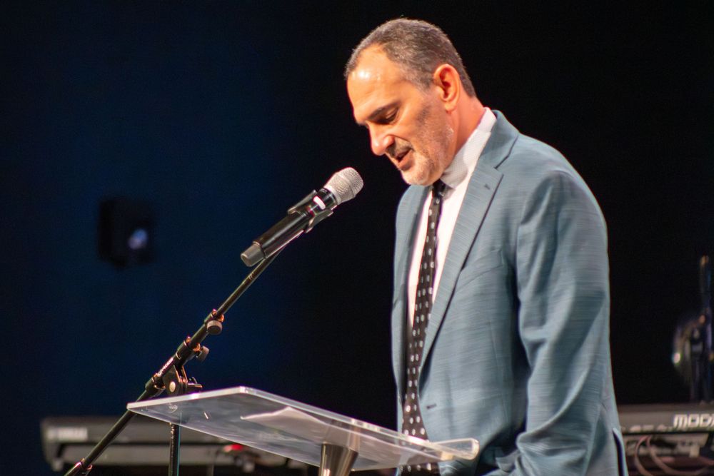 Presenter giving speech at podium with dark stage background.