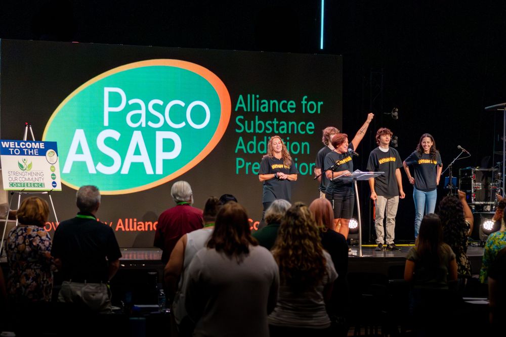 Conference stage setup with green organizational banners and audience seating visible.