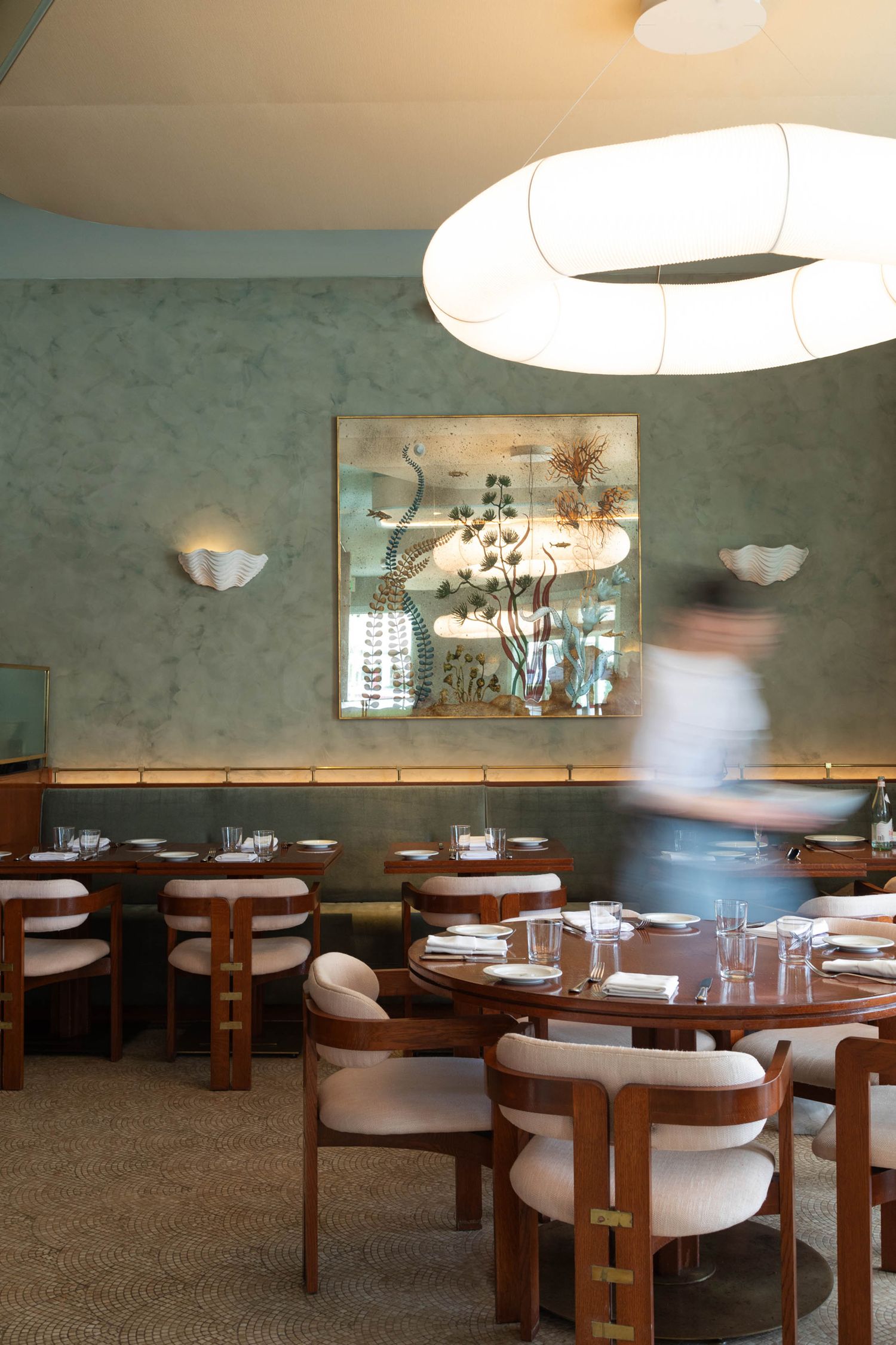 Beautiful restaurant interior with green walls, glass art, and a figure blurred, moving through the space.