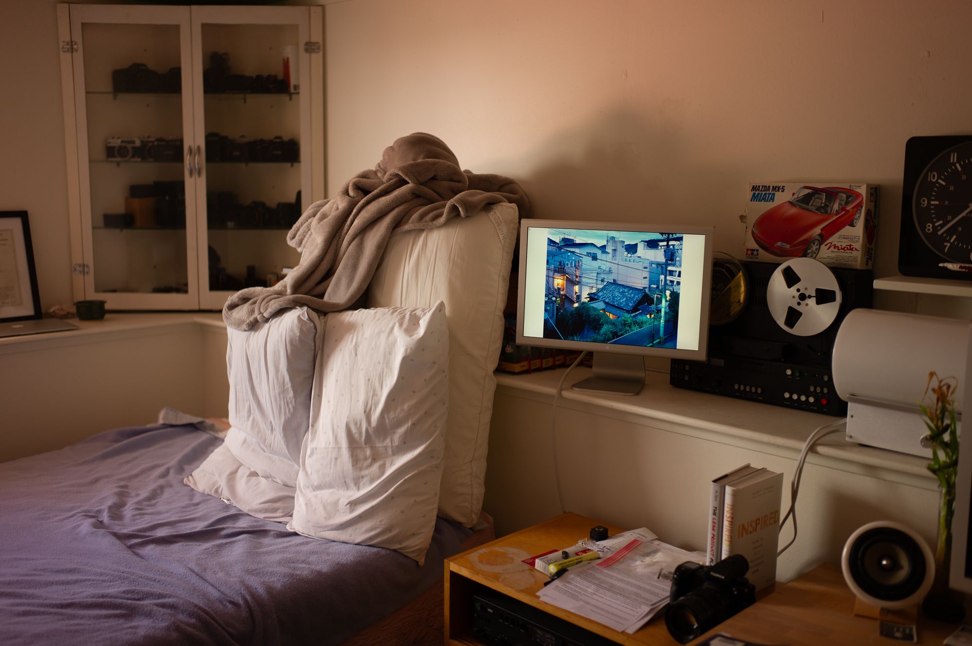 Person sitting on bed watching movie or gaming on small TV monitor in dark bedroom with purple bedspread.