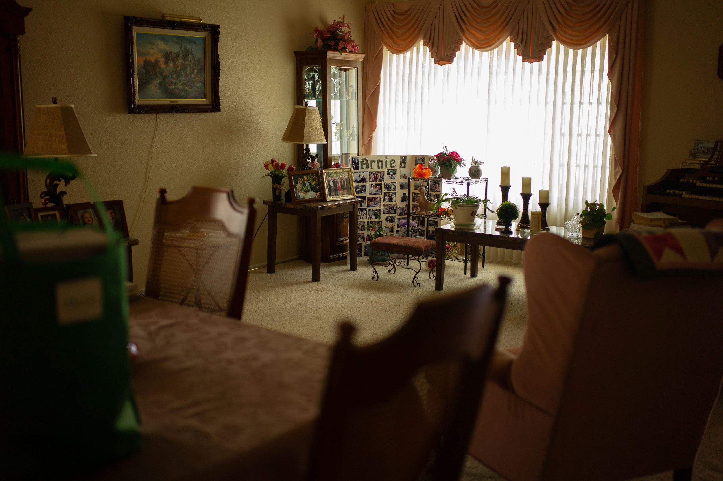 Interior view of a residential dining room with carpeted floor, furniture, and sunlit windows with decorative drapes.