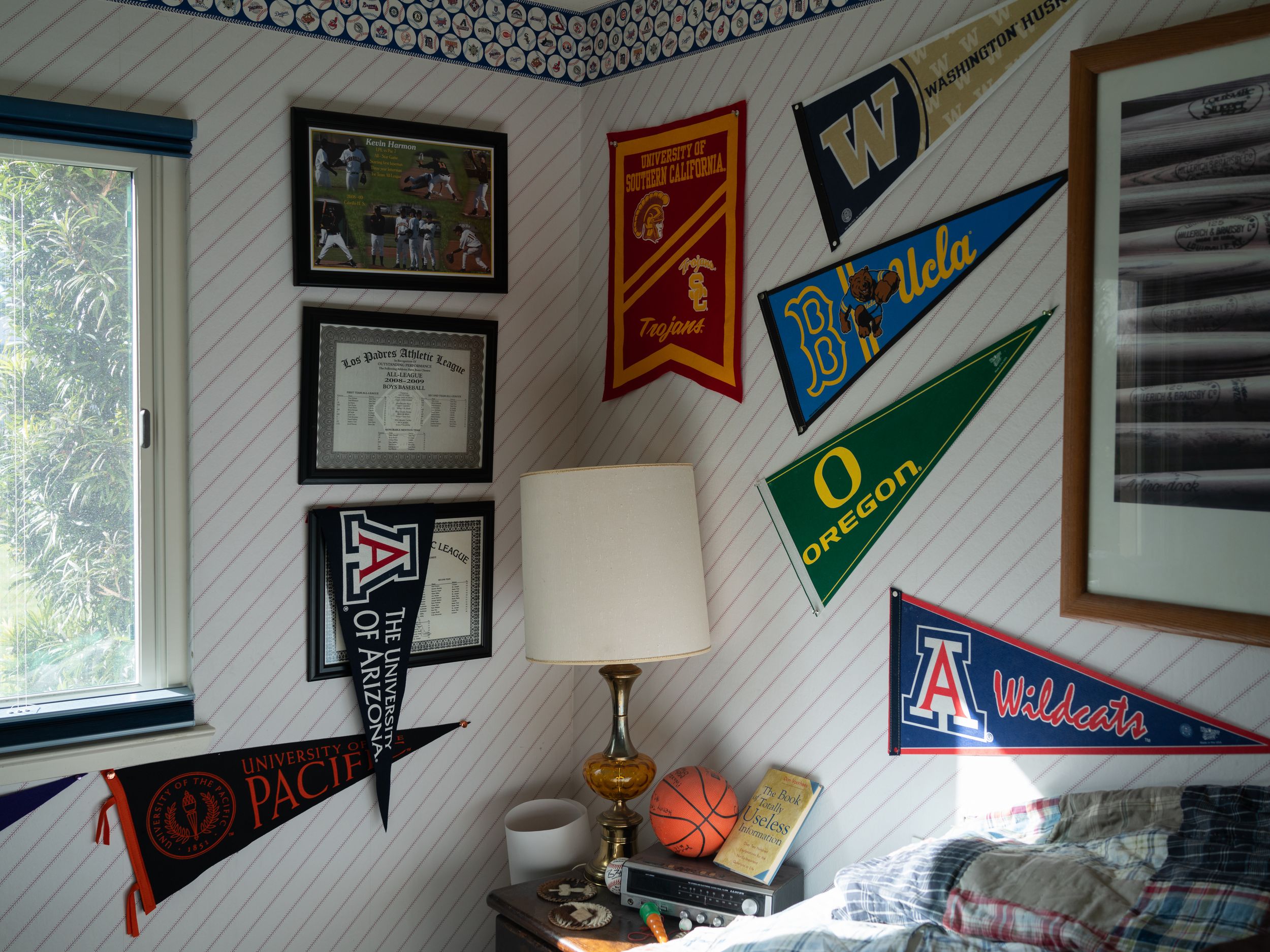 A dorm room corner decorated with collegiate pennants and flags from various universities displayed on white walls.