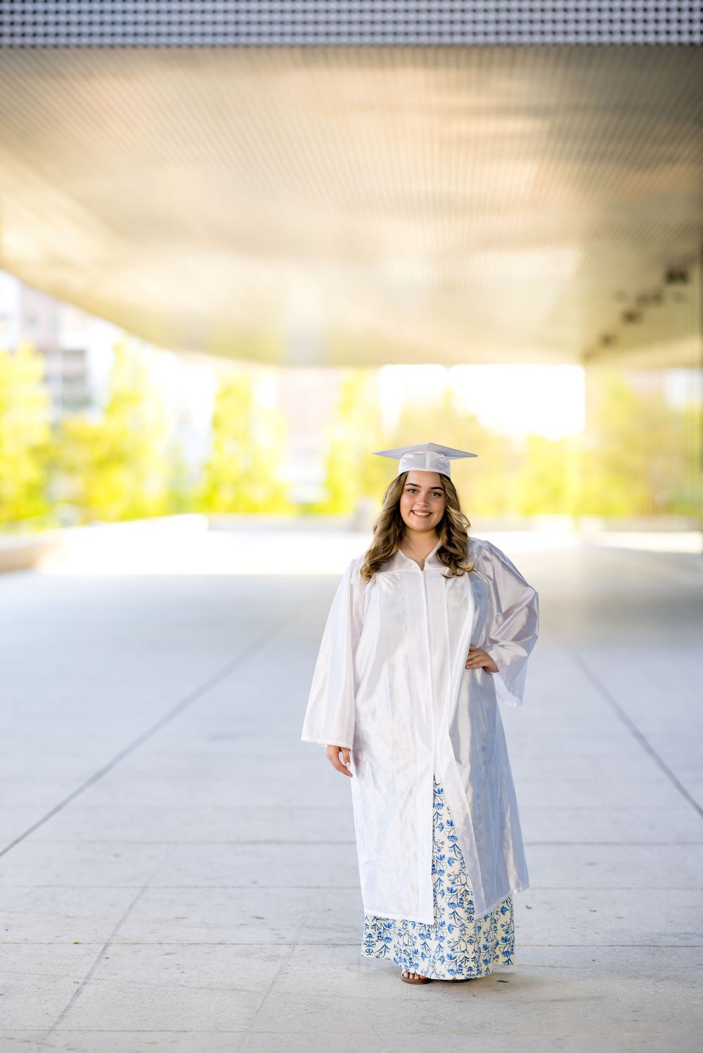 Graduate in white cap and gown walking during golden hour photoshoot.
