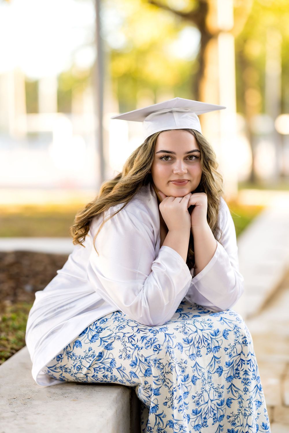 Graduate in white cap and gown posing on ground during outdoor photo session. Photos by Tampa Photographer DigitalMyst Photography