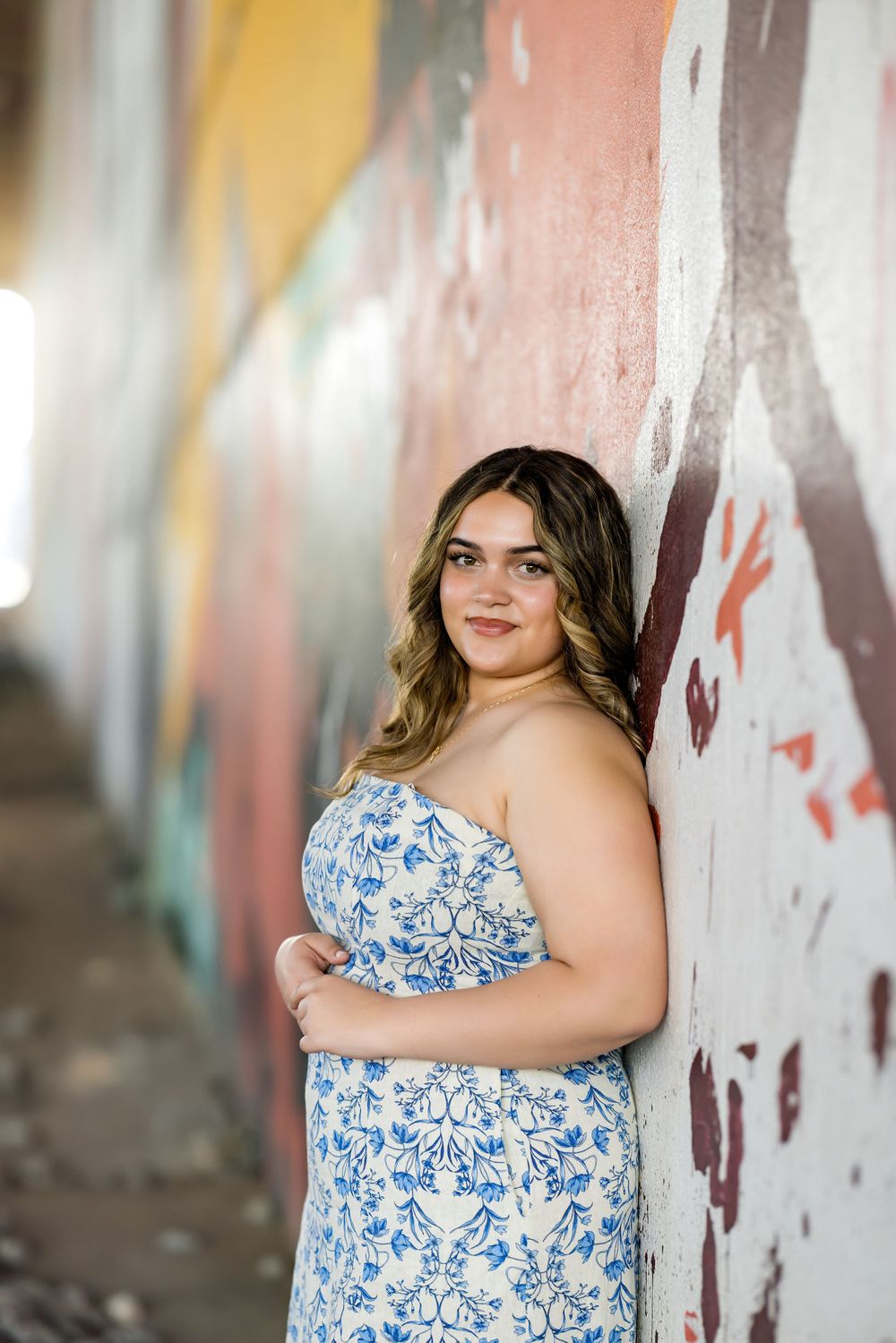 A casual pose against a painted wall wearing a blue floral dress.