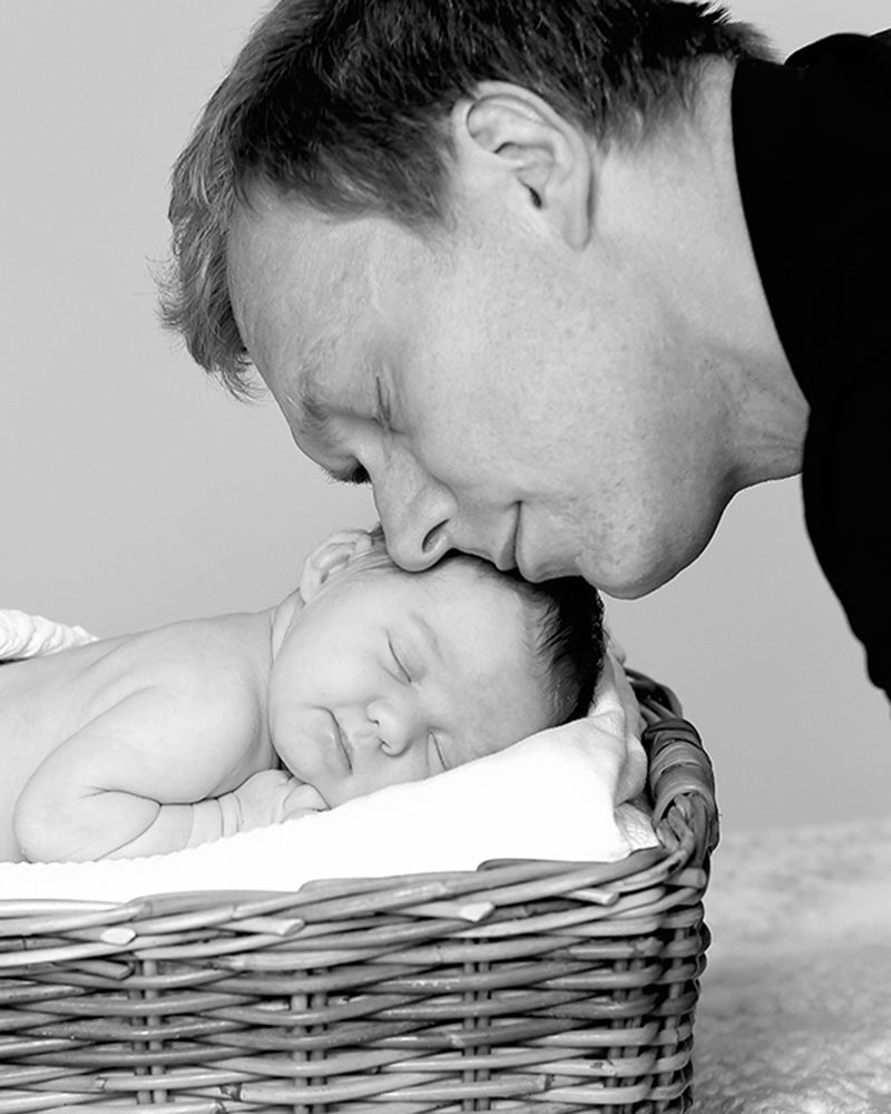 A father kisses his newborn daughter in a basket, showcasing a heartwarming moment of love, photographed by Abigail's Studio.