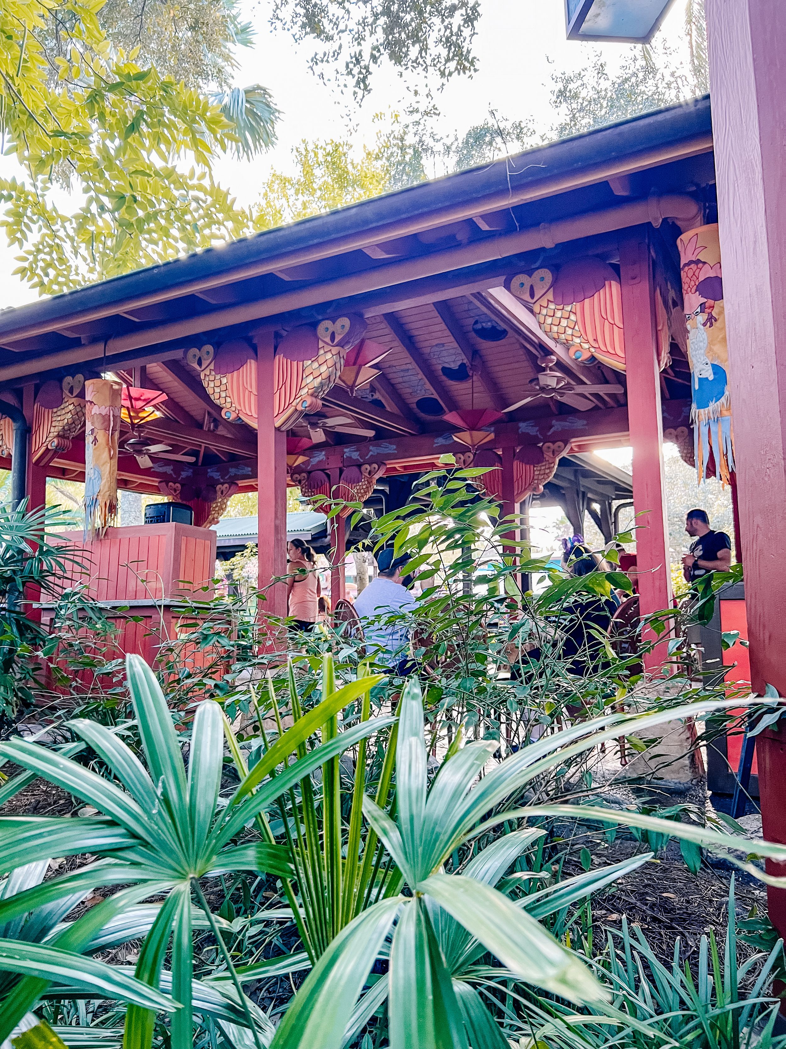 Garden patio with wooden beams and tropical plants creating a lush, serene outdoor space under leafy canopy.