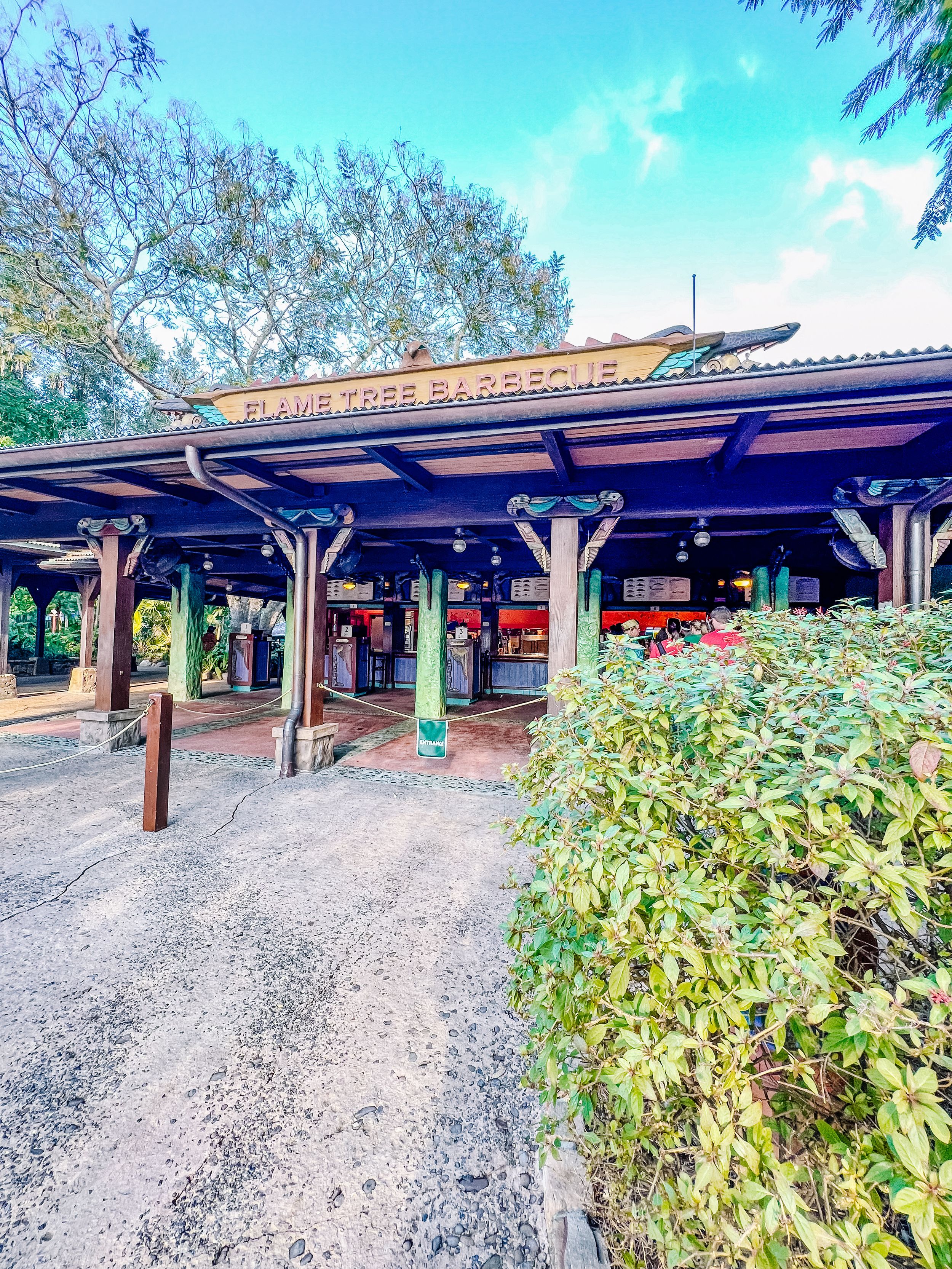 A rustic wooden train station platform with covered waiting area and decorative landscaping at Magic Kingdom park.