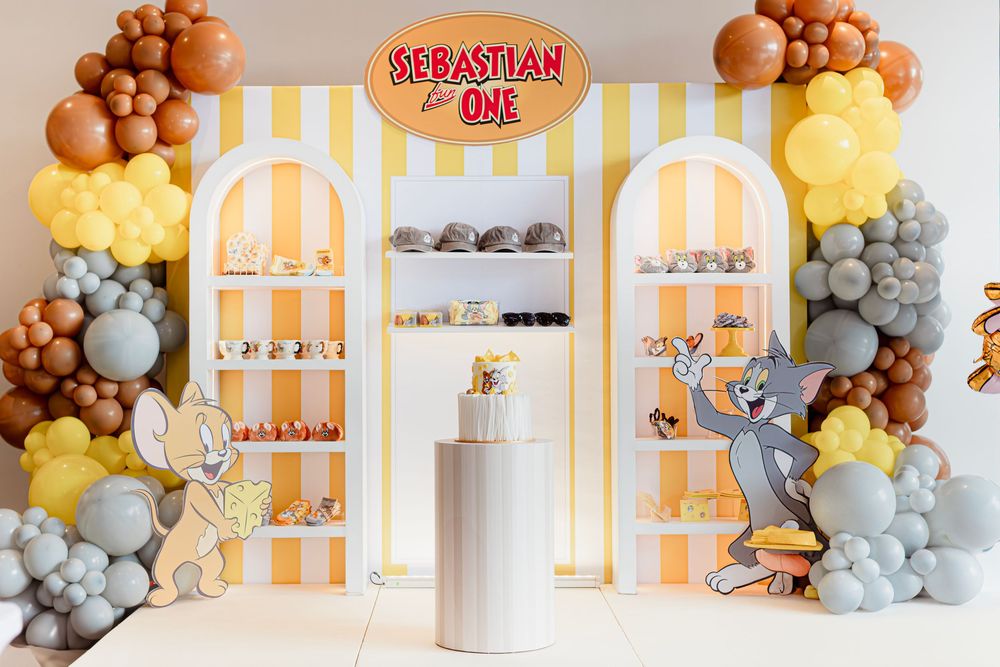 Tom and Jerry themed birthday party setup with yellow striped backdrop and balloon garland decorations.