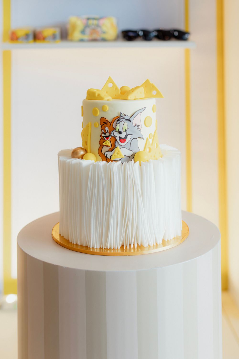 White fondant cake decorated with Tom and Jerry cartoon characters and yellow accents on a white pedestal.