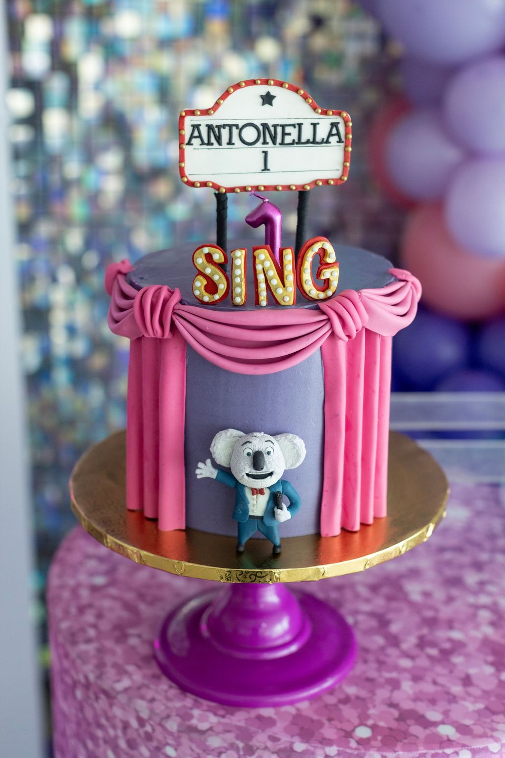 Pink theater-style cake with SING theme featuring a koala character and Antonella name topper.
